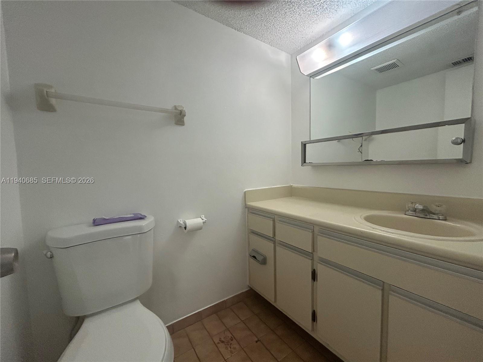 A bathroom features a white toilet, a vanity with a beige countertop, and a mirror — 5851 W 20th Ave # 409, Hialeah FL 33012, HIALEAH, FL