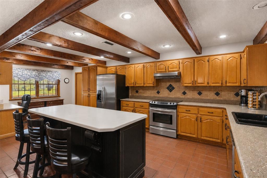 A kitchen and dining area with wood-beam ceilings, wooden cabinets, and terracotta tile flooring — 35841 TIMBERTOP LANE, FRUITLAND PARK, FL