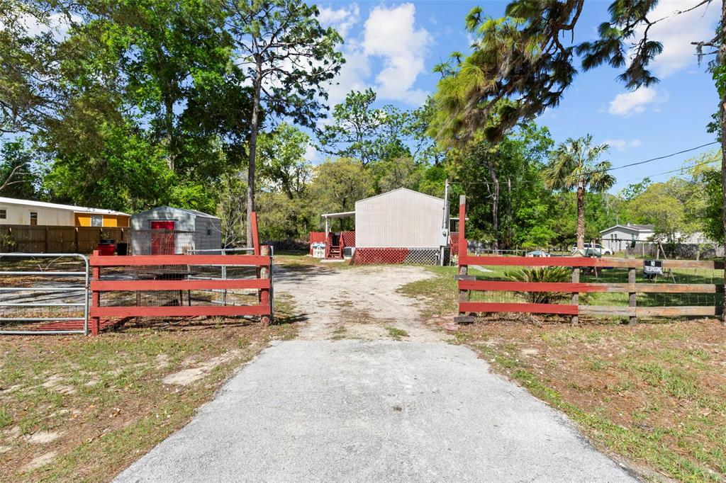 A gravel driveway leads to a mobile home behind a red wooden fence and gate — 3474 S ARUNDEL TERRACE, HOMOSASSA, FL