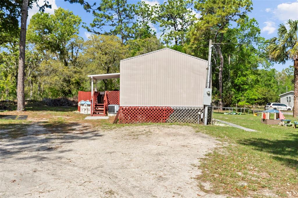 A side view of a manufactured home with a red lattice skirt and wooden porch — 3474 S ARUNDEL TERRACE, HOMOSASSA, FL