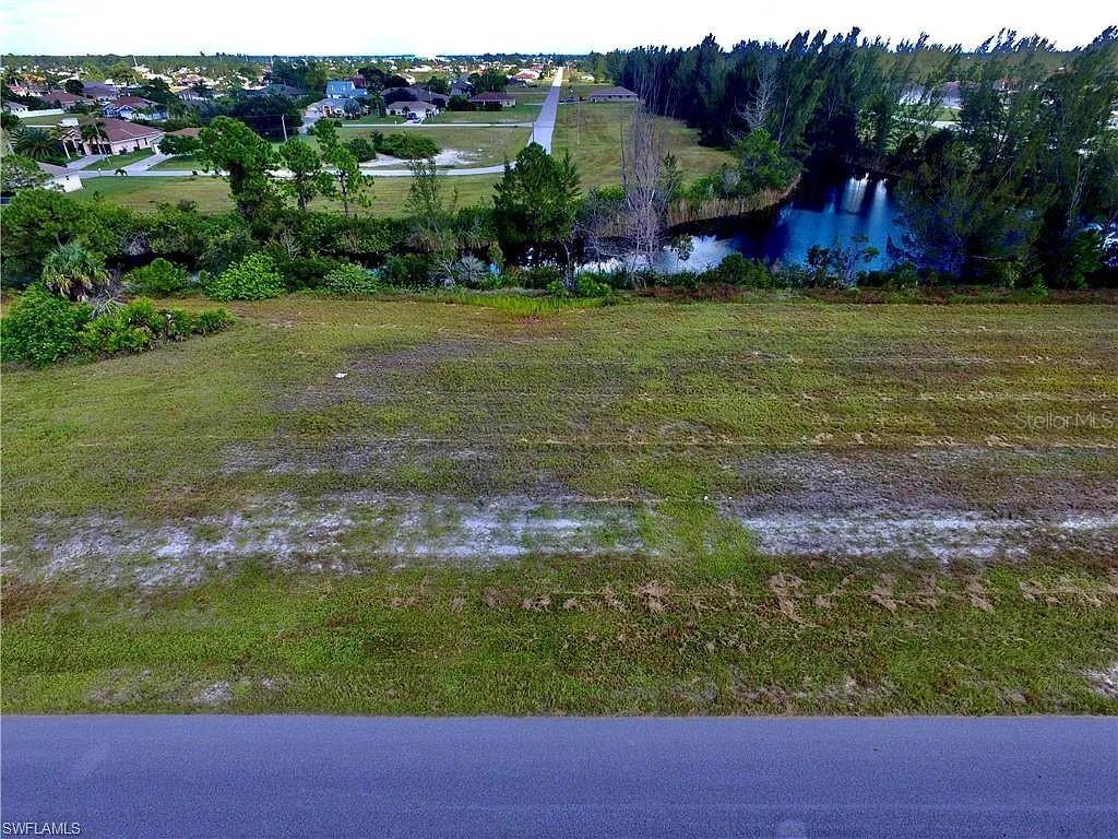 An aerial view shows a vacant, grassy lot bordering a small pond and residential neighborhood — 2017 NW 24TH AVENUE, CAPE CORAL, FL