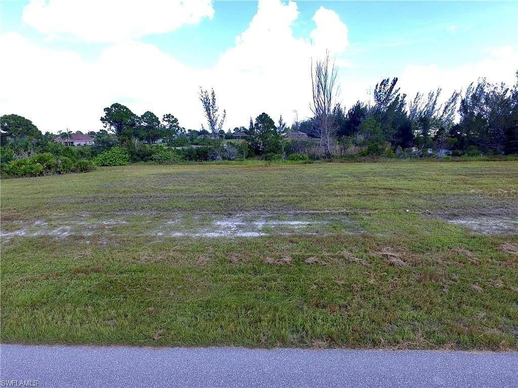 A flat, grassy vacant lot is viewed from the street under a cloudy sky — 2017 NW 24TH AVENUE, CAPE CORAL, FL