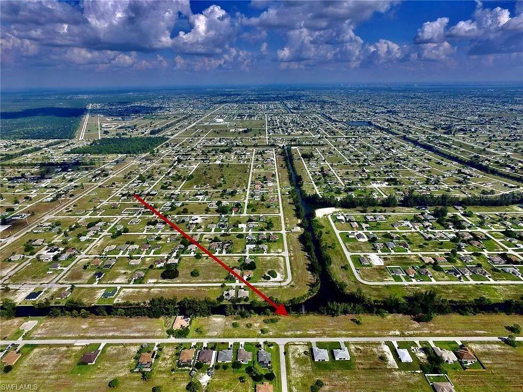 An aerial view shows a residential neighborhood with a canal and a red arrow pointing toward a vacant lot — 2017 NW 24TH AVENUE, CAPE CORAL, FL