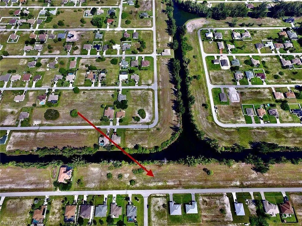An aerial view shows a vacant residential lot marked by a red arrow — 2017 NW 24TH AVENUE, CAPE CORAL, FL