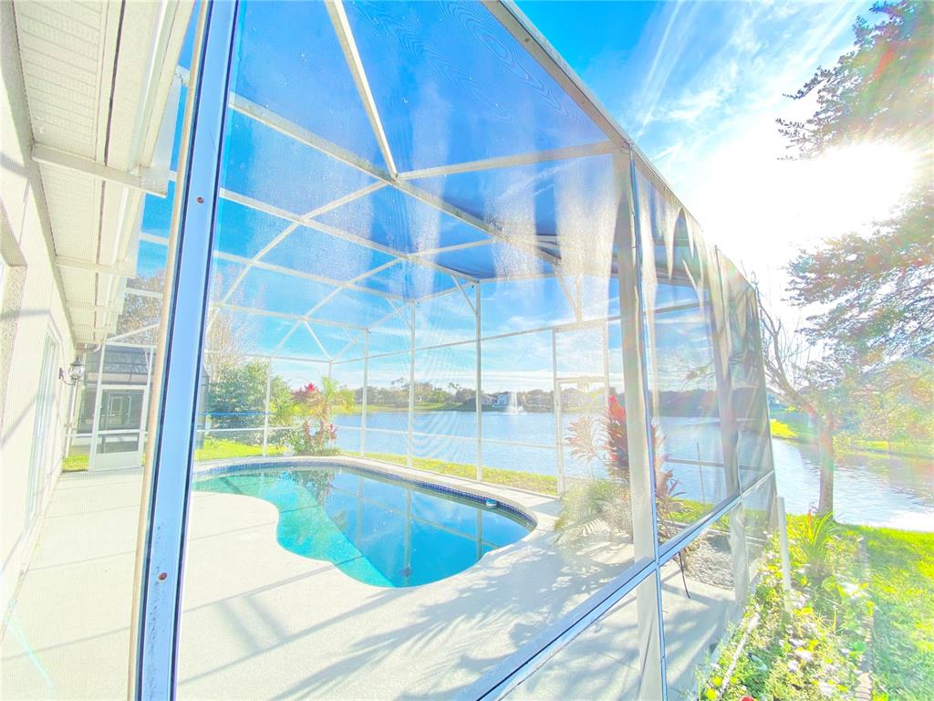 A screened-in pool enclosure overlooks a lake with a fountain on a sunny day — 729 TUTEN TRAIL, ORLANDO, FL