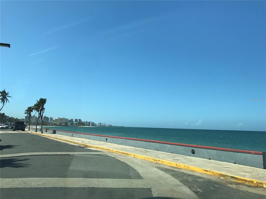 A coastal road runs alongside a concrete seawall overlooking the ocean with a city skyline — 7 GUERRERO NOBLE UNIT 3, SAN JUAN, PR
