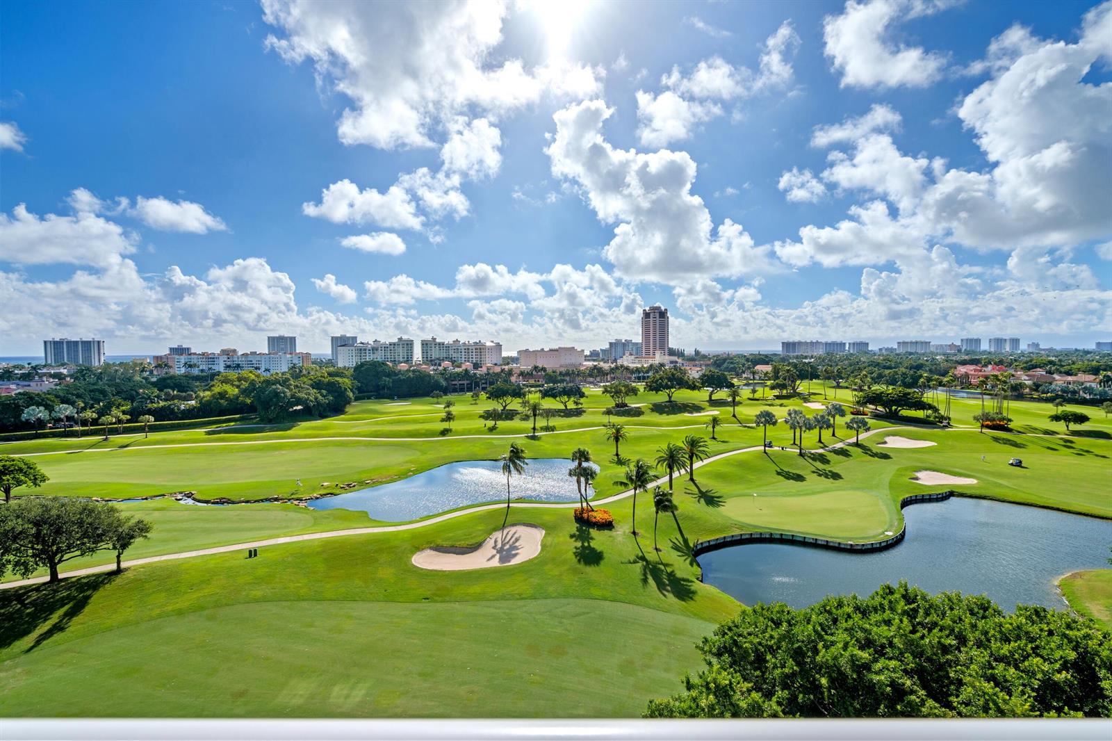 An elevated view of a lush green golf course with ponds, palm trees, and city buildings — 220 SE Mizner Boulevard # 24, Boca Raton FL 33432, BOCA RATON, FL