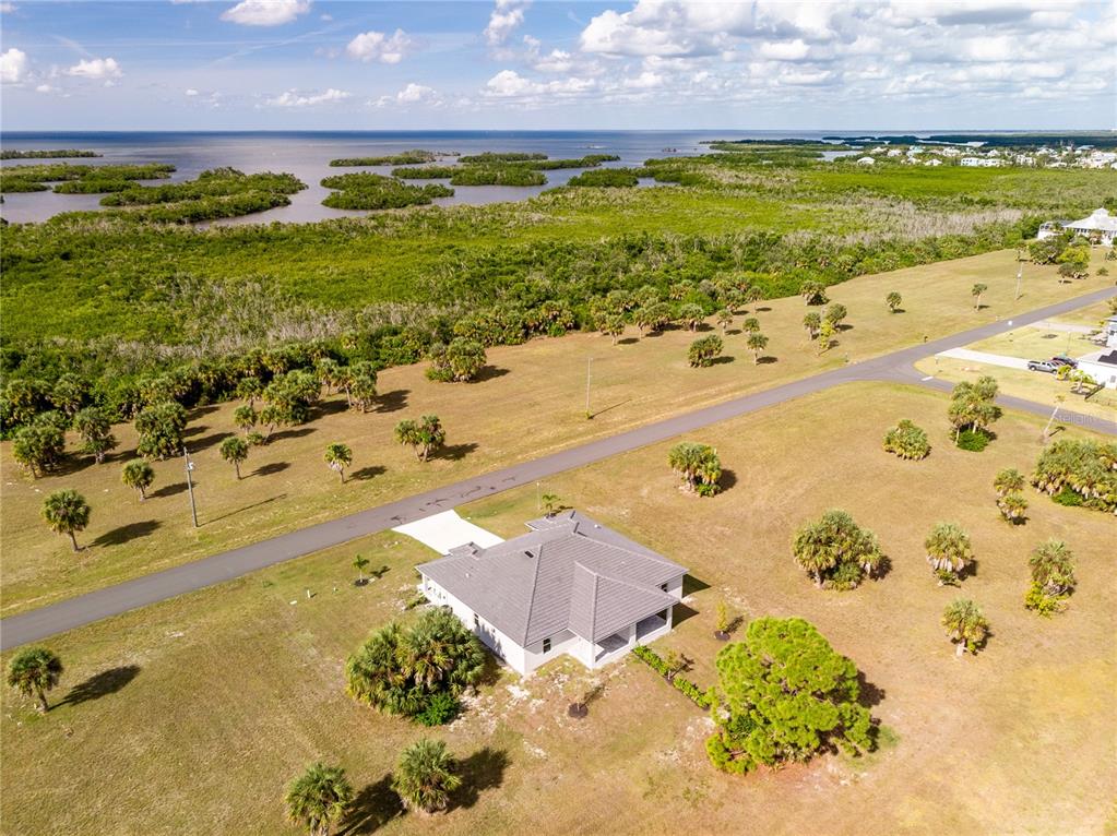 An aerial view shows a single-story house situated on a large, grassy lot near water — 16810/16812 SAN EDMUNDO ROAD, PUNTA GORDA, FL