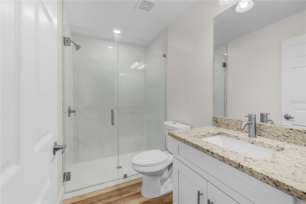 A bathroom features a glass-enclosed shower, a white toilet, and a granite-topped vanity — 16810/16812 SAN EDMUNDO ROAD, PUNTA GORDA, FL