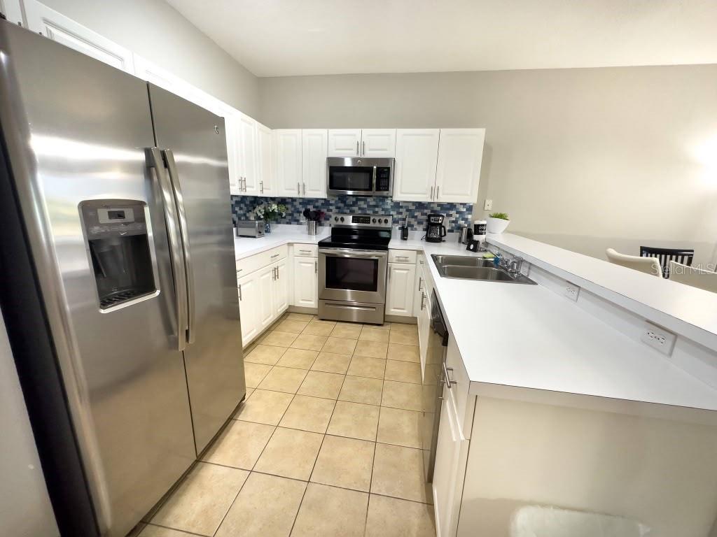 A kitchen features white cabinets, stainless steel appliances, a tiled backsplash, and light-colored countertops — 3137 SUN LAKE COURT UNIT A, KISSIMMEE, FL