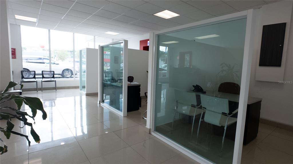 An office space features glass-walled cubicles, white tile flooring, and large windows overlooking a parking lot — San Agustin AVE 65TH INFANTERIA, SAN JUAN, PR