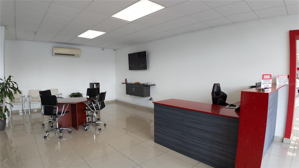 An office interior features a red reception desk, a conference table, and a wall-mounted television — San Agustin AVE 65TH INFANTERIA, SAN JUAN, PR