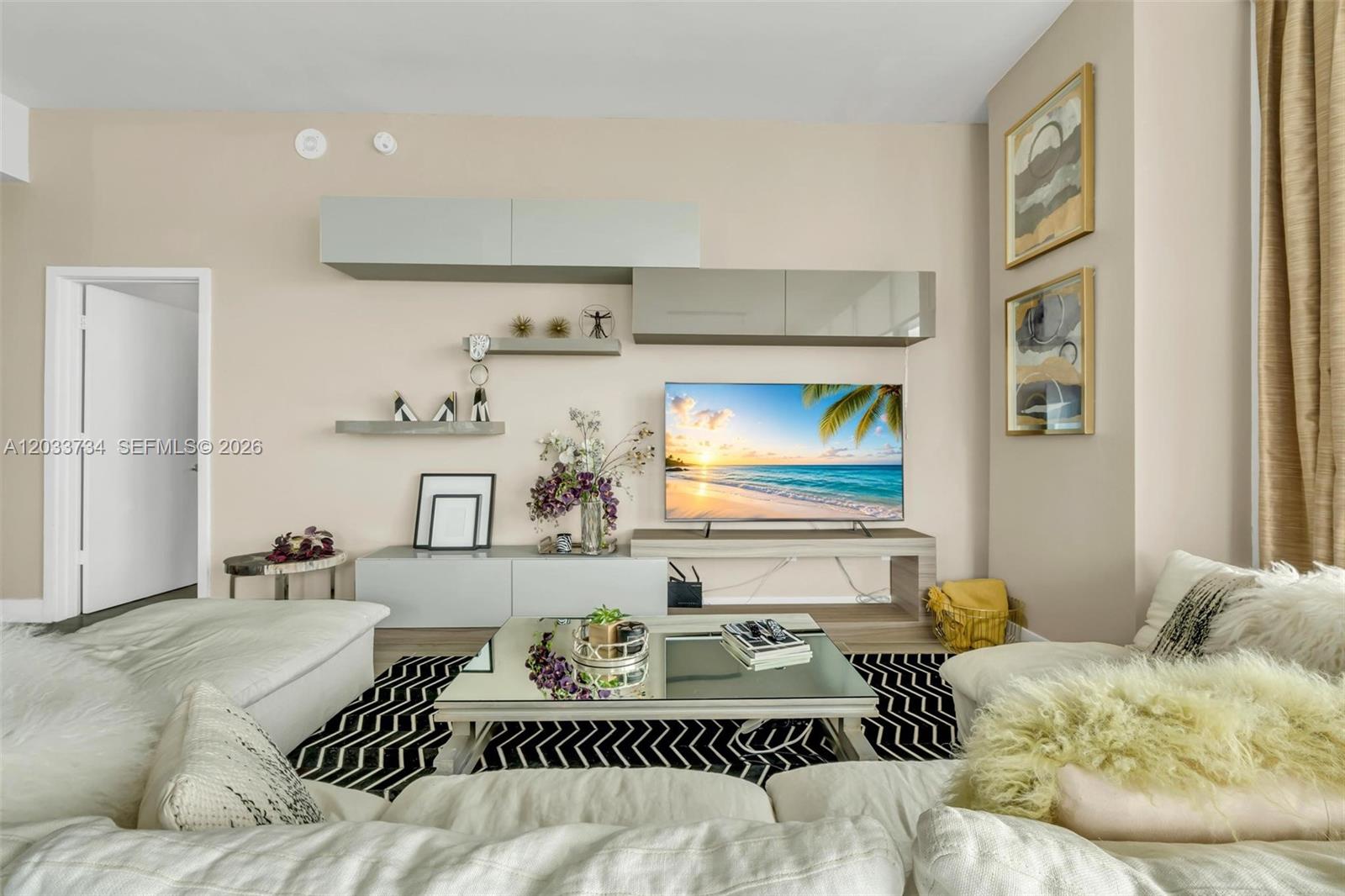 A living room features a wall-mounted entertainment unit, a mirrored coffee table, and white sofas — 1300 S Miami Ave, Miami FL 33130, MIAMI, FL