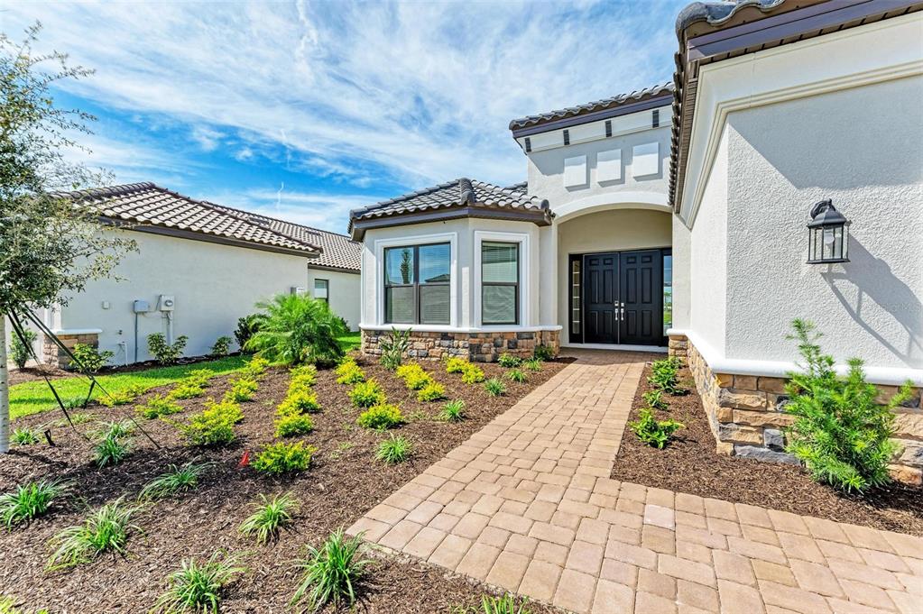 A paved walkway leads to the double front doors of a stucco house with stone accents — 16403 UMBRIA PLACE, BRADENTON, FL
