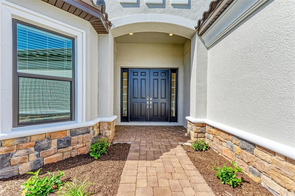 A paved walkway leads to the double front doors of a house with stone siding — 16403 UMBRIA PLACE, BRADENTON, FL