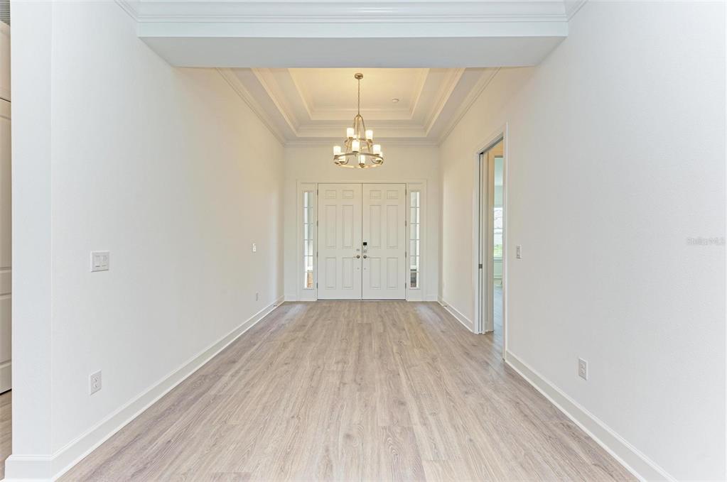 A bright entryway features light wood-look flooring, a tray ceiling with a chandelier, and double doors — 16403 UMBRIA PLACE, BRADENTON, FL
