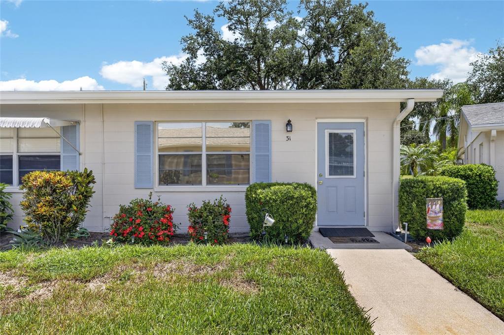 A single-story house exterior features a light-colored facade, blue shutters, and a blue front door — 402 DORCHESTER PLACE UNIT 31, SUN CITY CENTER, FL