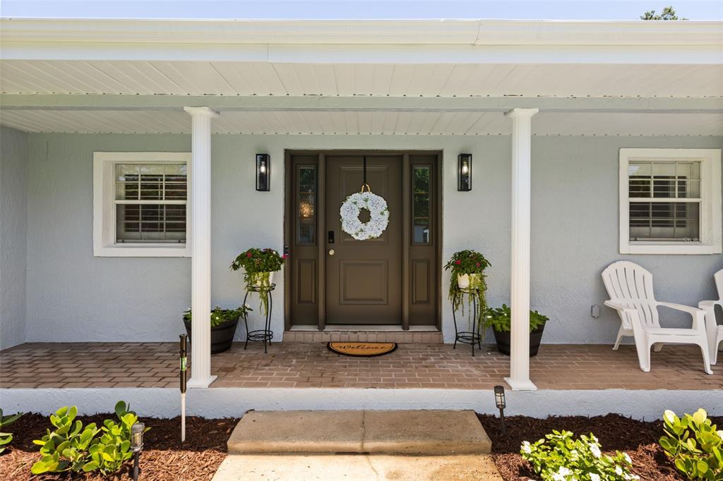 A light blue house exterior features a covered brick porch with white columns and chairs — 1871 BARKER DRIVE, WINTER PARK, FL