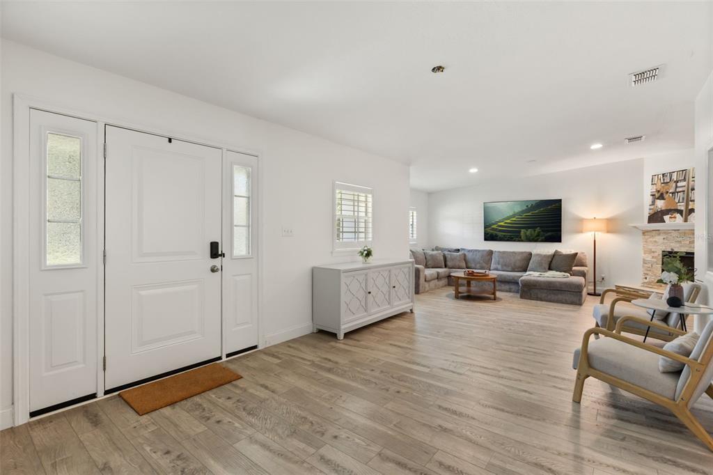 A bright living room features light wood flooring, a white console table, and a sectional sofa — 1871 BARKER DRIVE, WINTER PARK, FL