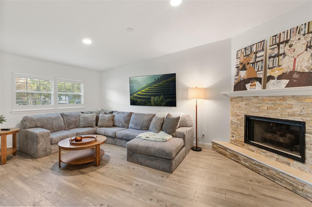 A living room features a gray sectional sofa, a stone fireplace, and light wood flooring — 1871 BARKER DRIVE, WINTER PARK, FL