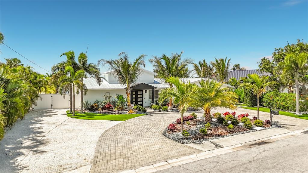 A white house with a metal roof features a paved driveway and tropical landscaping — 605 KEY ROYALE DRIVE, HOLMES BEACH, FL