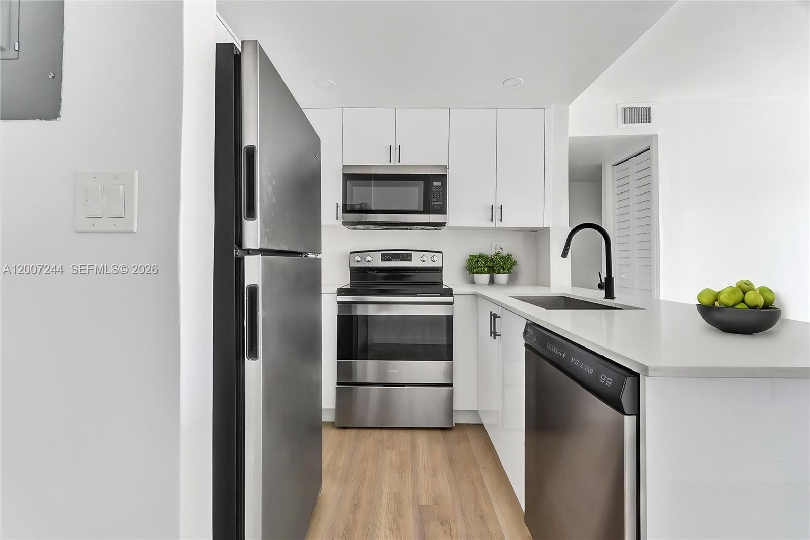 A modern kitchen features white cabinets, stainless steel appliances, and light wood-look flooring — 620 SW 10th St # 301, Miami FL 33130, MIAMI, FL