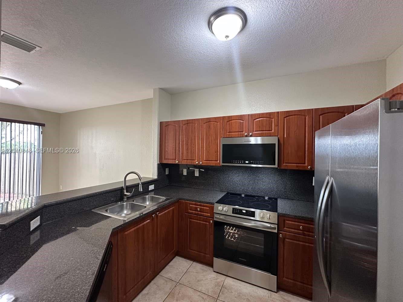 A kitchen features wood cabinets, dark granite countertops, stainless steel appliances, and tile flooring — MIAMI, FL