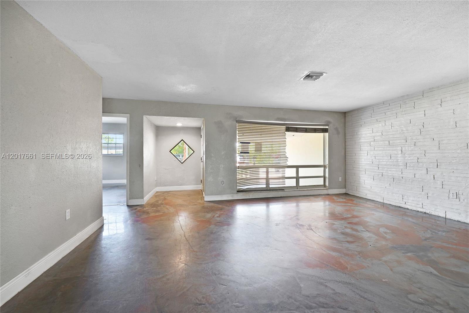 A living room features stained concrete floors, a white brick wall, and a large window — 7773 Biltmore Blvd, Miramar FL 33023, MIRAMAR, FL