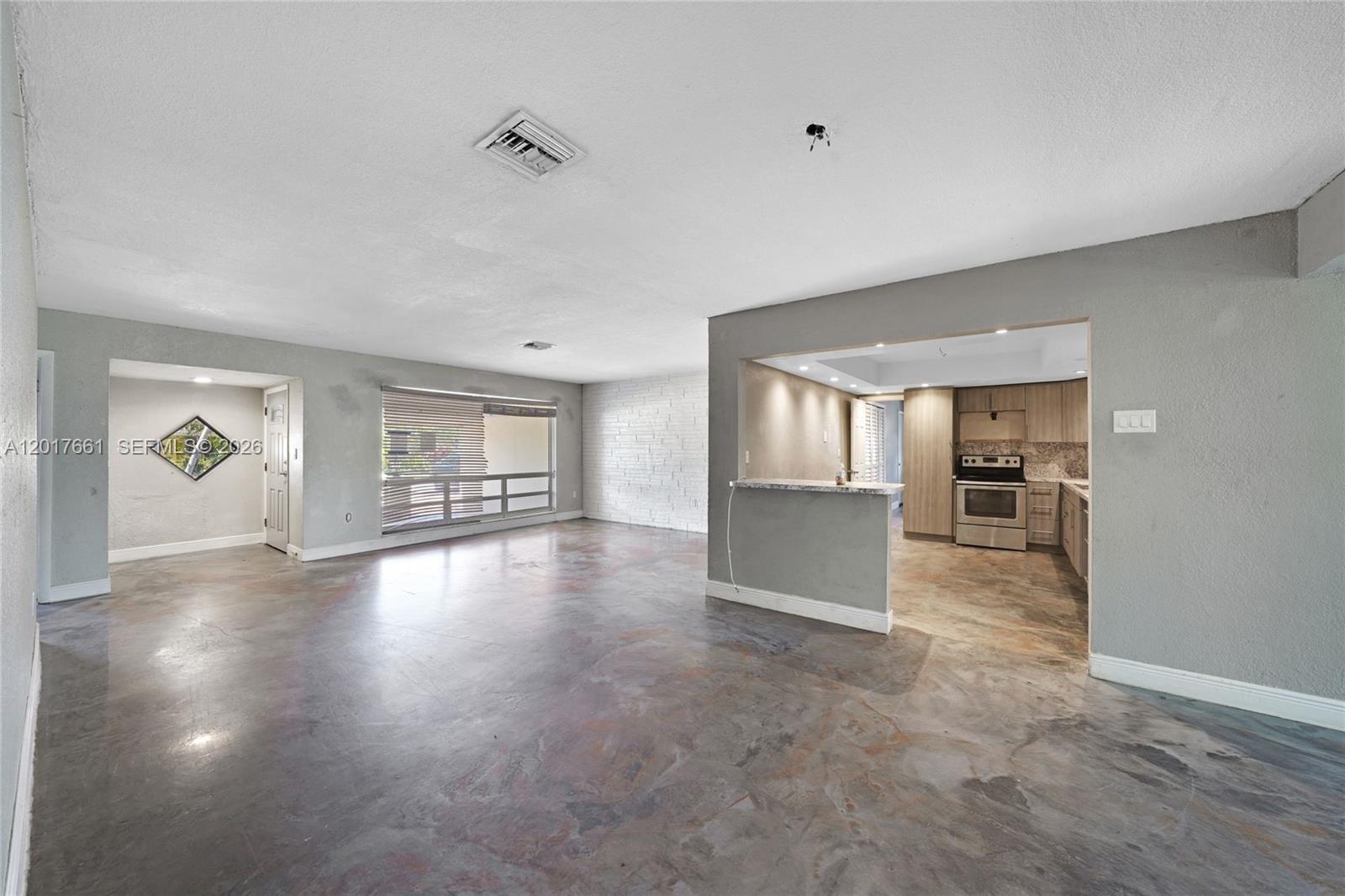An open-concept living area features polished concrete floors, a kitchen pass-through, and a white brick wall — 7773 Biltmore Blvd, Miramar FL 33023, MIRAMAR, FL
