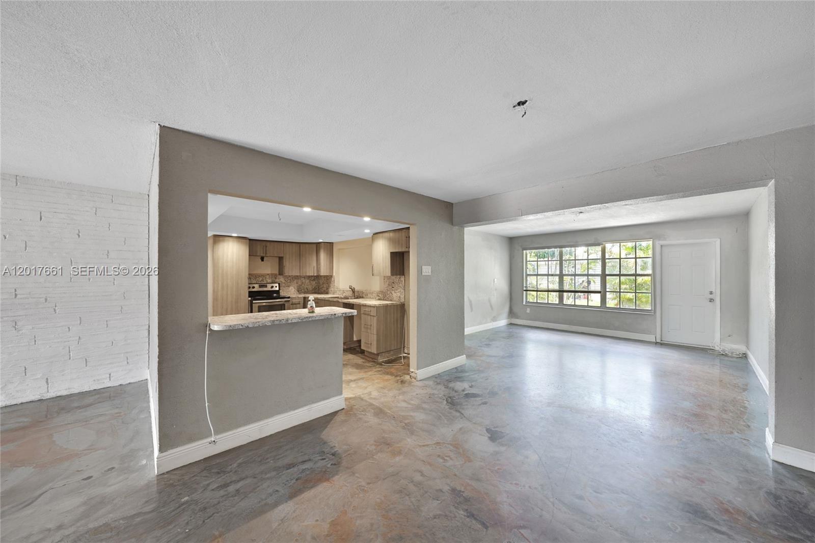 An open-concept living area features polished concrete floors, a kitchen pass-through, and a white door — 7773 Biltmore Blvd, Miramar FL 33023, MIRAMAR, FL