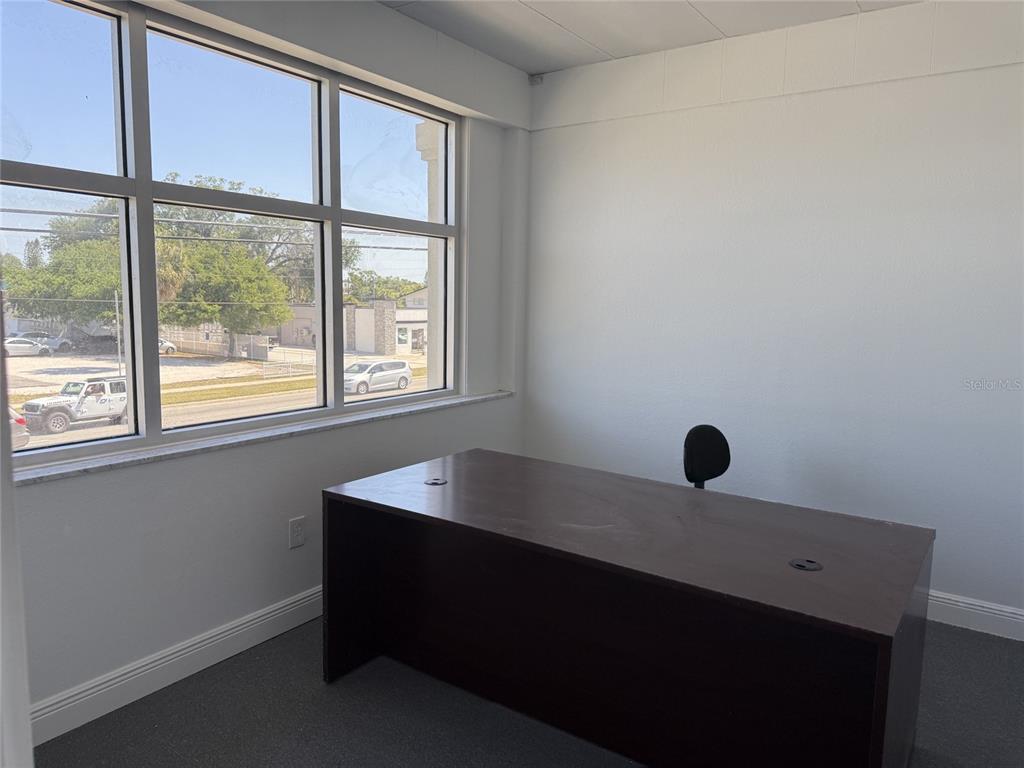 A small office features a dark wood desk, gray carpet, and large windows overlooking parking — 501 S LINCOLN AVENUE UNIT 22, CLEARWATER, FL