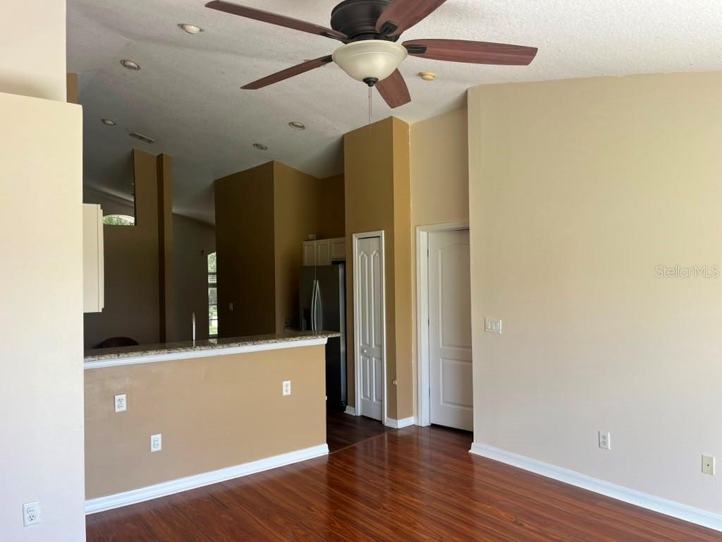 A living area with wood-look flooring, a ceiling fan, and an open kitchen counter — 30918 STONE ARCH AVENUE, WESLEY CHAPEL, FL