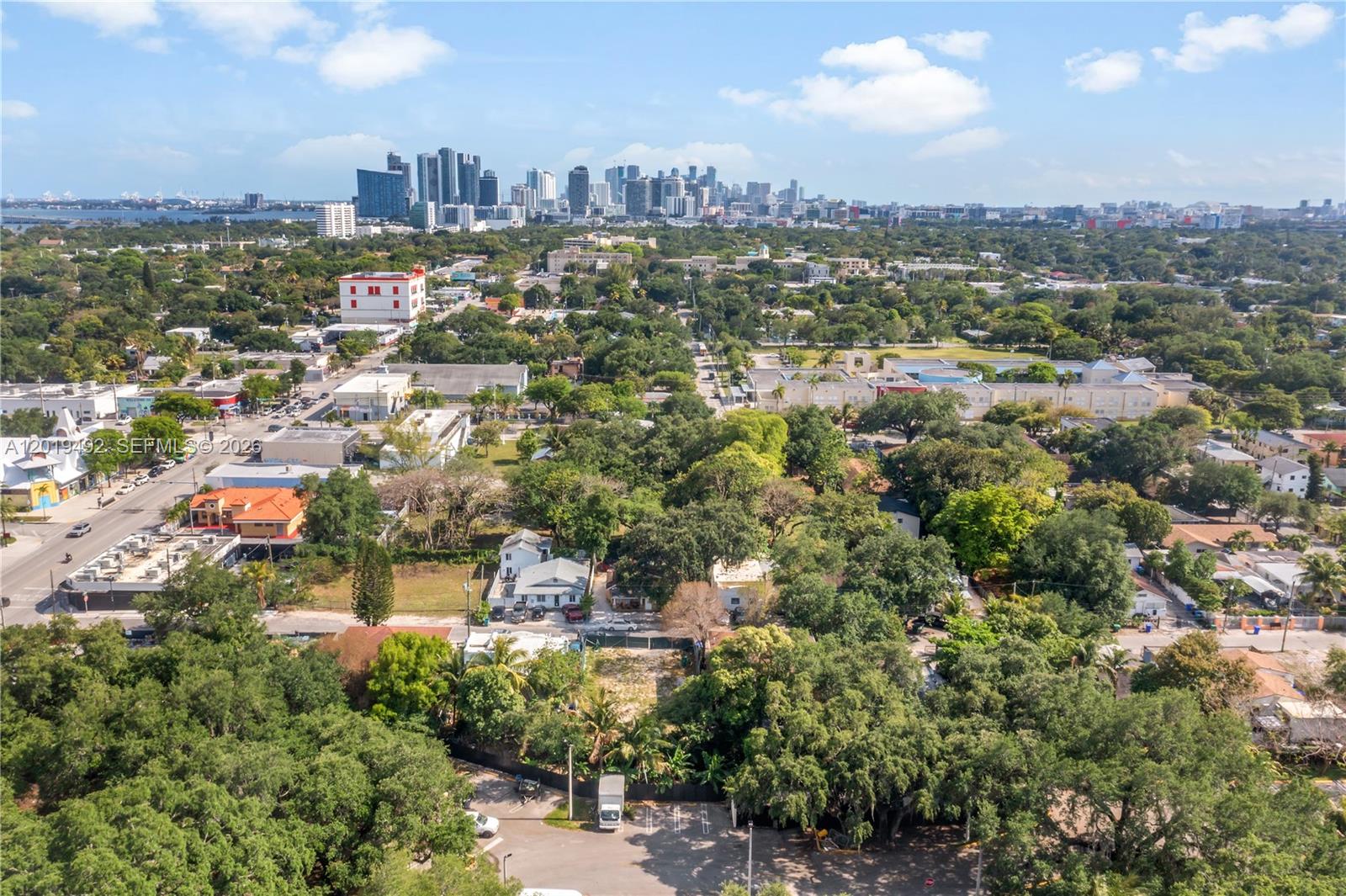 An aerial view shows a residential neighborhood with dense trees and a distant city skyline — 161 NE 60th St, Miami FL 33137, MIAMI, FL