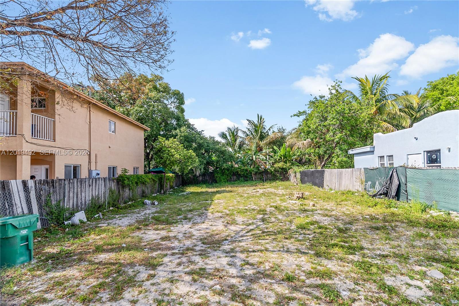 A vacant, dirt-covered lot sits between two residential buildings with wooden fences on both sides — 161 NE 60th St, Miami FL 33137, MIAMI, FL