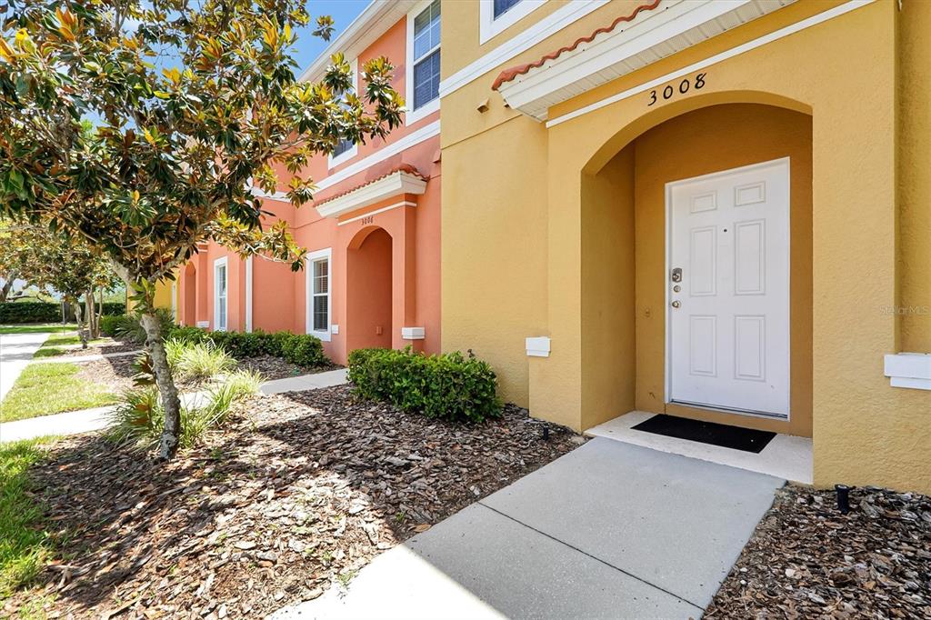 The exterior of a yellow and orange multi-story townhouse with a white front door — 3008 RED GINGER ROAD UNIT 3008, KISSIMMEE, FL