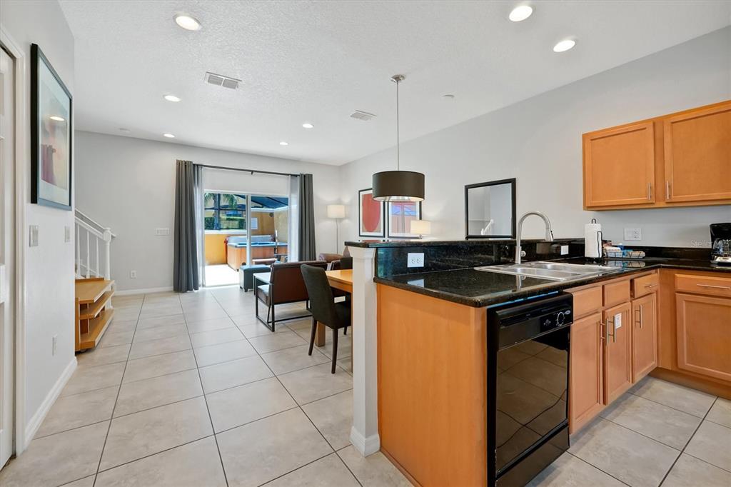 A kitchen with wood cabinets and black countertops overlooks a dining and living area — 3008 RED GINGER ROAD UNIT 3008, KISSIMMEE, FL
