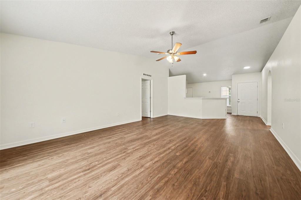A spacious living room with wood-look flooring, white walls, and a ceiling fan — 909 BRISTLE CONE COURT, MINNEOLA, FL