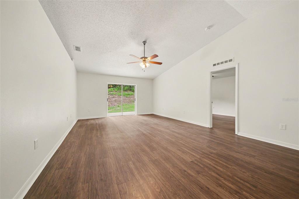An empty living room with wood-look flooring, a ceiling fan, and sliding glass doors — 909 BRISTLE CONE COURT, MINNEOLA, FL