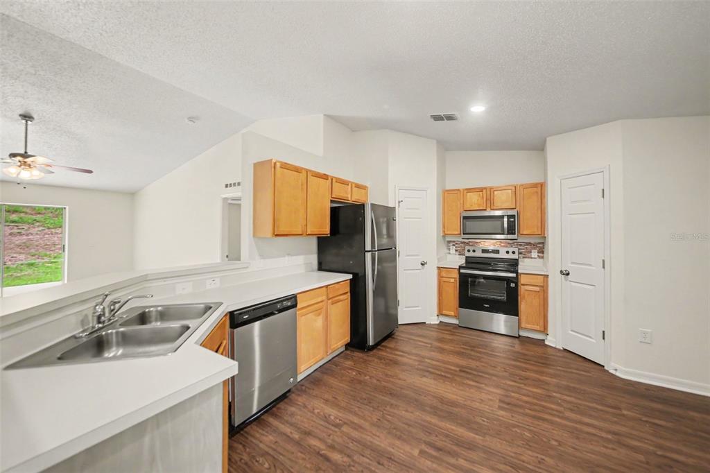 A kitchen features light wood cabinets, stainless steel appliances, and dark wood-look flooring — 909 BRISTLE CONE COURT, MINNEOLA, FL