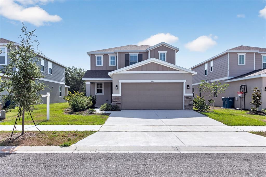 A two-story suburban house with a tan exterior, a two-car garage, and a concrete driveway — 821 BLUE CREEK DRIVE, HAINES CITY, FL