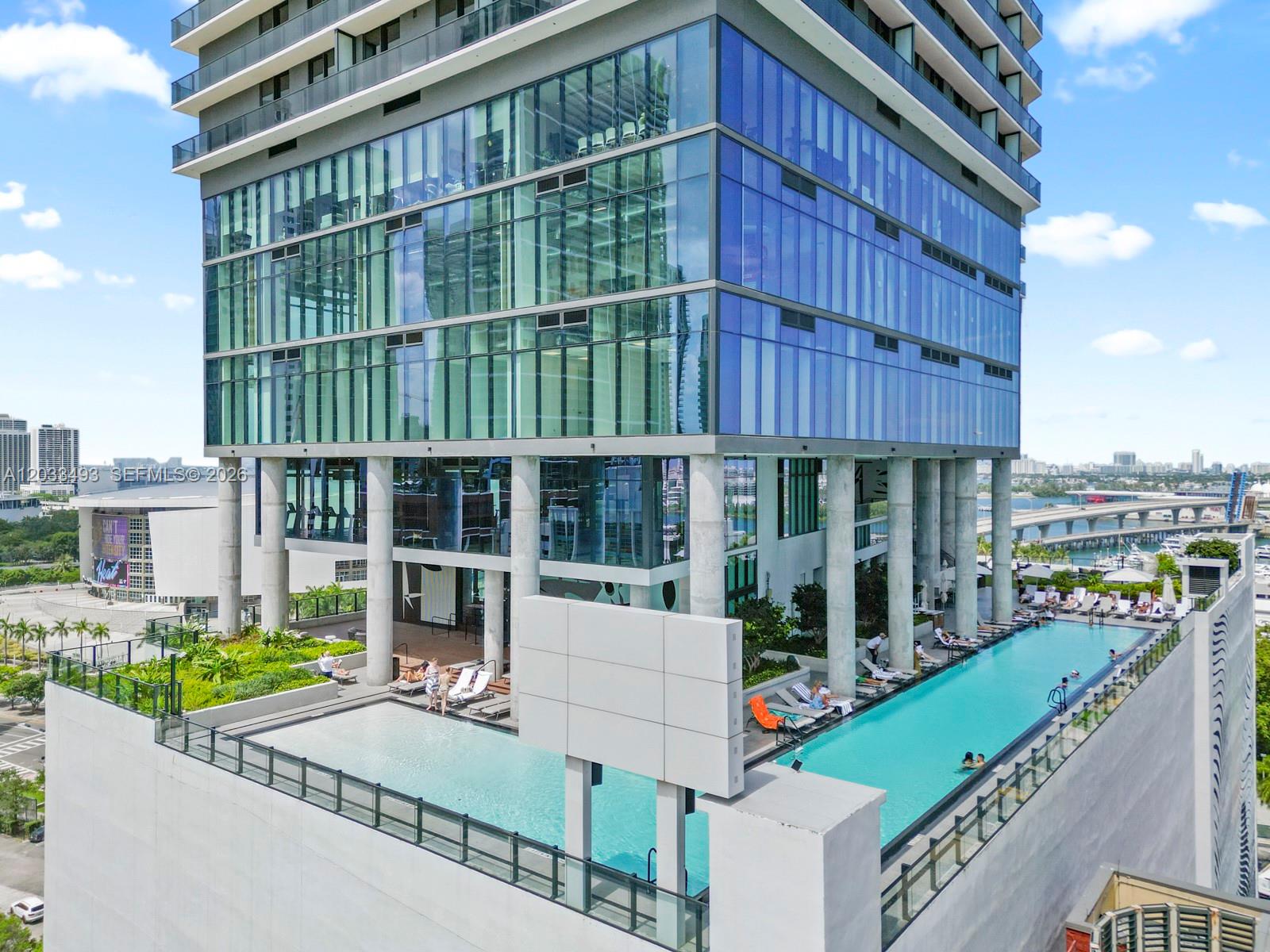 An elevated outdoor swimming pool with lounge chairs sits on a terrace beneath a glass skyscraper — 398 NE 5th St # 3318, Miami FL 33132, MIAMI, FL