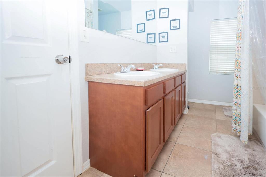 A bathroom features a double-sink vanity with wood cabinets, a beige countertop, and tiled floors — 1132 CARLTON STREET, CLEARWATER, FL
