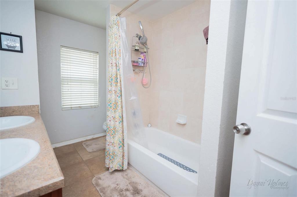 A bathroom features a double vanity, a tiled shower-tub combination, and a window with blinds — 1132 CARLTON STREET, CLEARWATER, FL