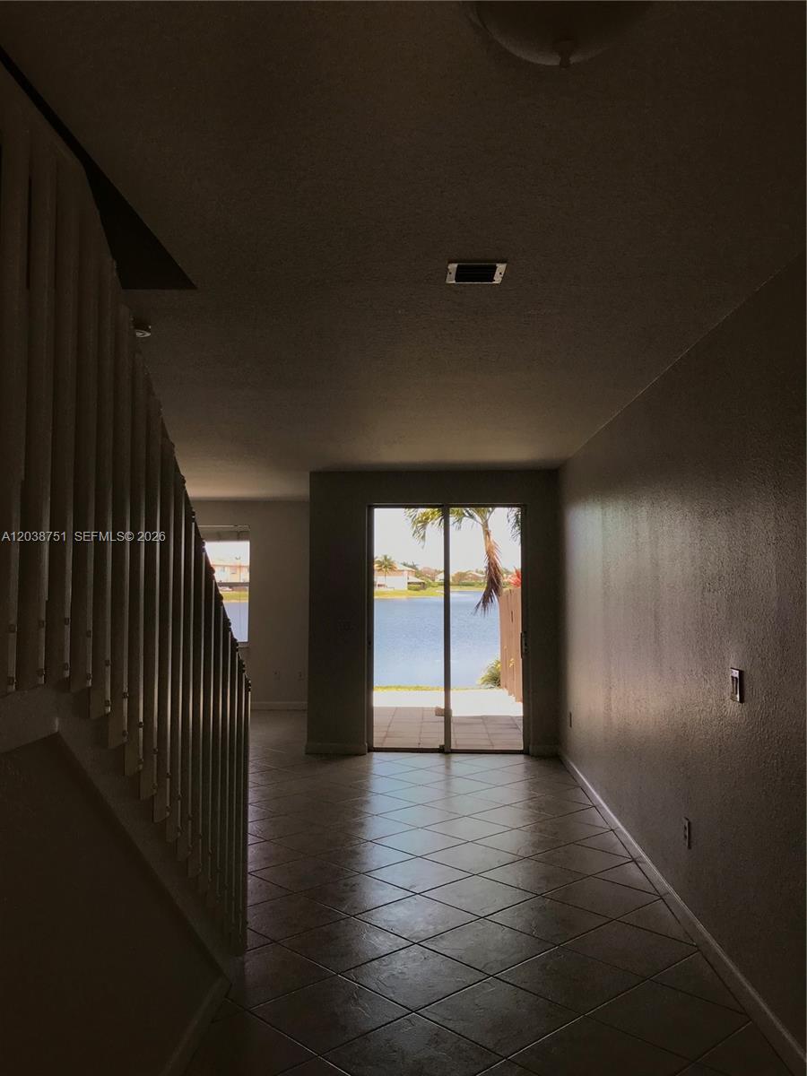 A tiled hallway leads to a sliding glass door with a view of a lake — 6674 NW 107th Pl, Doral FL 33178, DORAL, FL