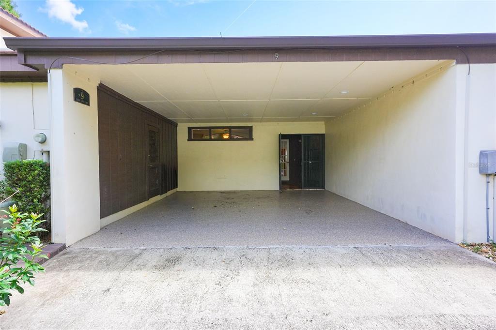 A covered carport with a concrete floor, a brown wood-paneled wall, and a front entrance — 9 CASA LOMA WAY UNIT 9, LAKELAND, FL