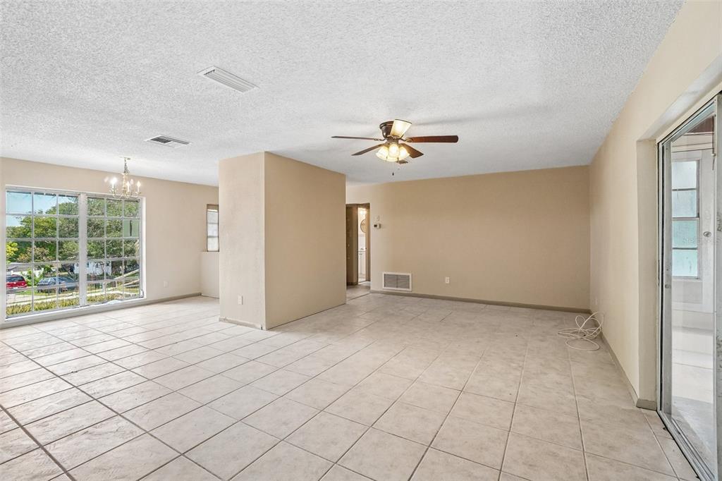 A spacious, empty living room with beige tile flooring, a ceiling fan, and large windows — 1090 EDGEHILL AVE, SPRING HILL, FL