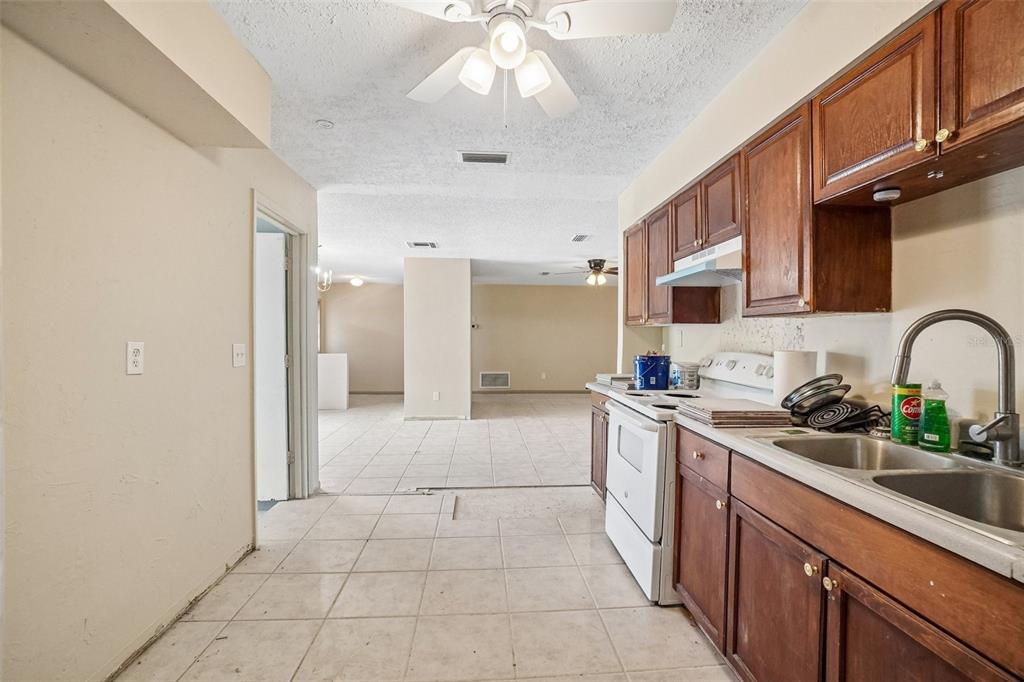 A kitchen with brown cabinets and tile flooring opens into a large, empty living area — 1090 EDGEHILL AVE, SPRING HILL, FL