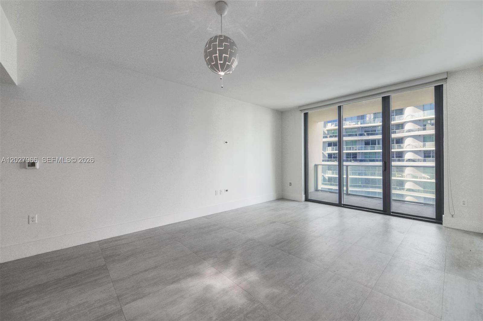An empty room features gray tile flooring, white walls, a modern pendant light, and balcony access — 1010 Brickell Ave # 4607, Miami FL 33131, MIAMI, FL