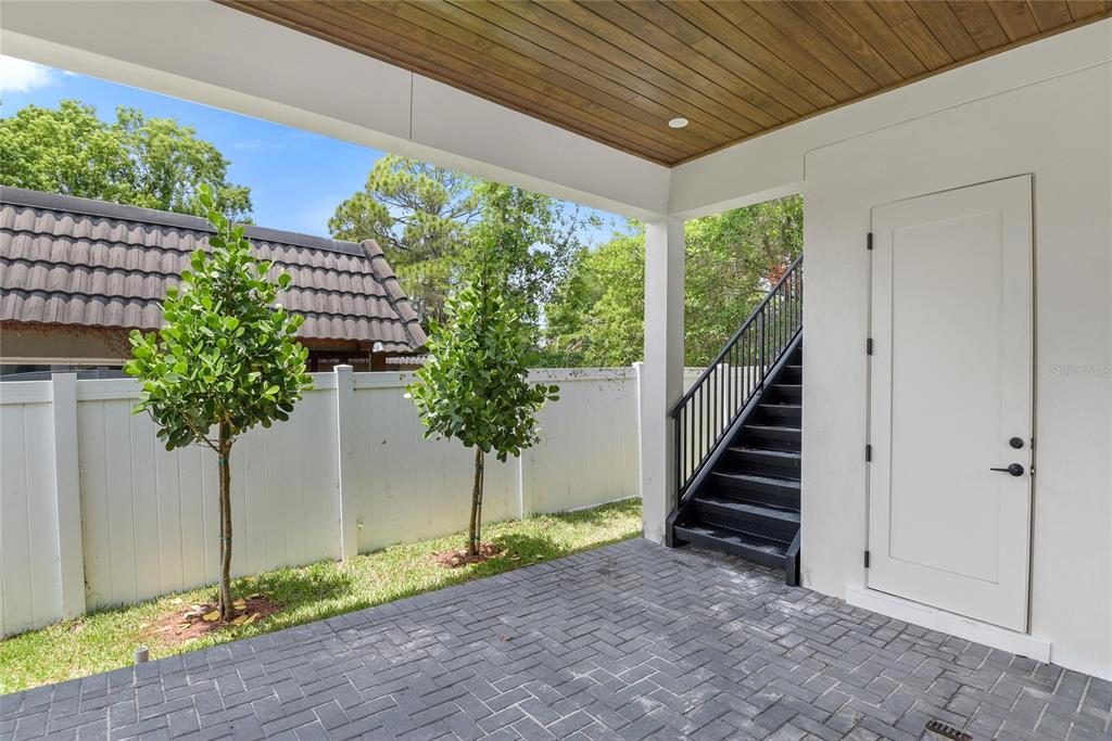 A covered patio features gray brick pavers, two small trees, and an exterior black staircase — 3222 HOLLIDAY AVE, APOPKA, FL
