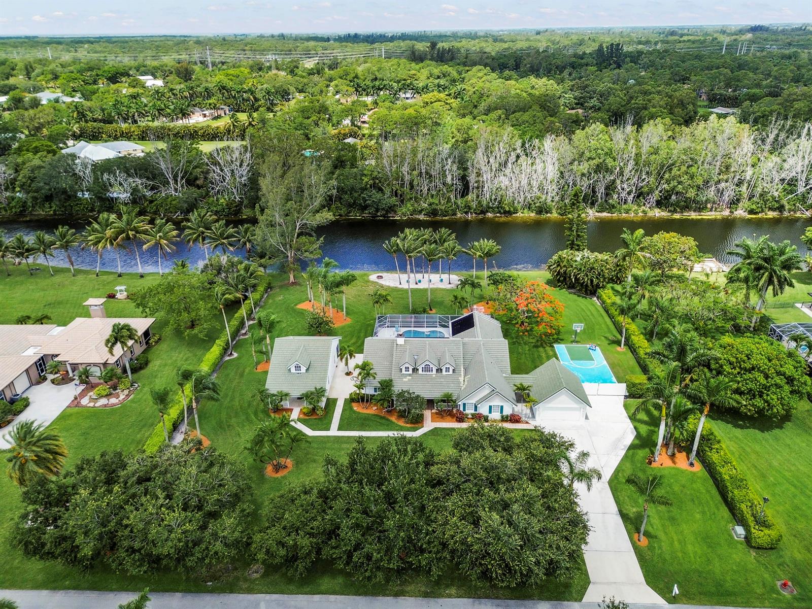 An aerial view shows a large house with a pool, basketball court, and expansive lawn — 5637 Lago Del Sol Drive, Lake Worth FL 33449, LAKE WORTH, FL